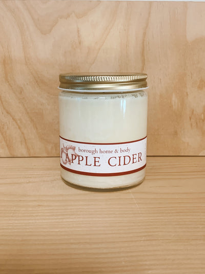 Apple Cider scented candle against a neutral wooden background.