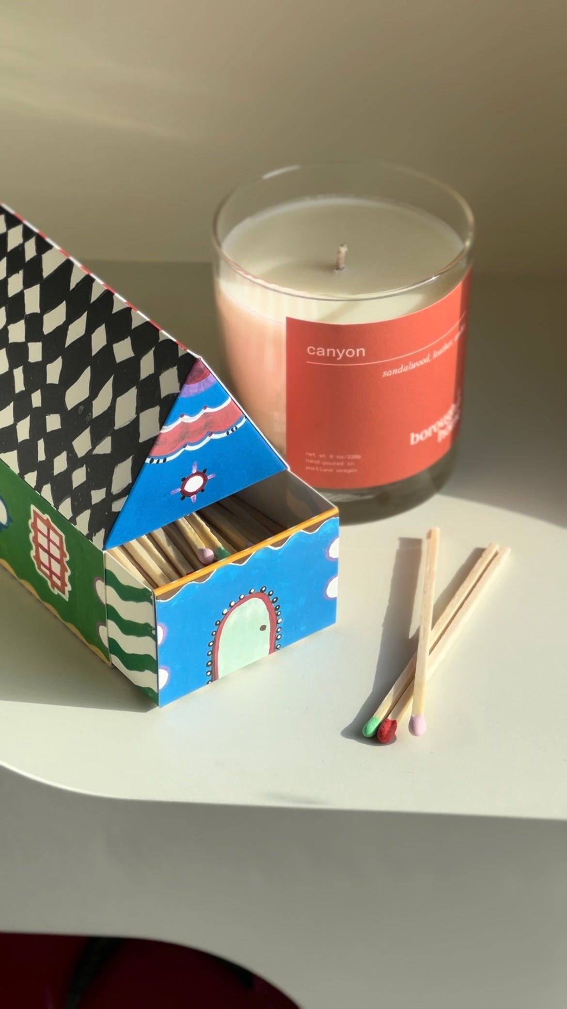 Box of House matches next to a soy wax candle, top down view