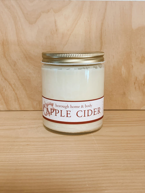 Apple Cider scented candle against a neutral wooden background.