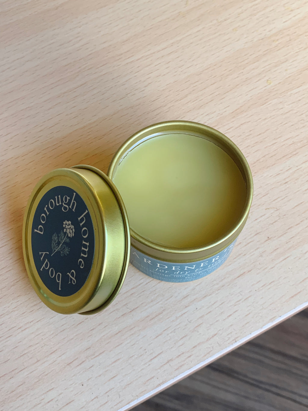 Open tin of 'Borough Home & Body' balm on a wooden surface