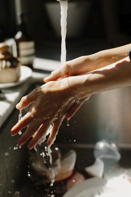 Person washing hands under running water in a kitchen setting