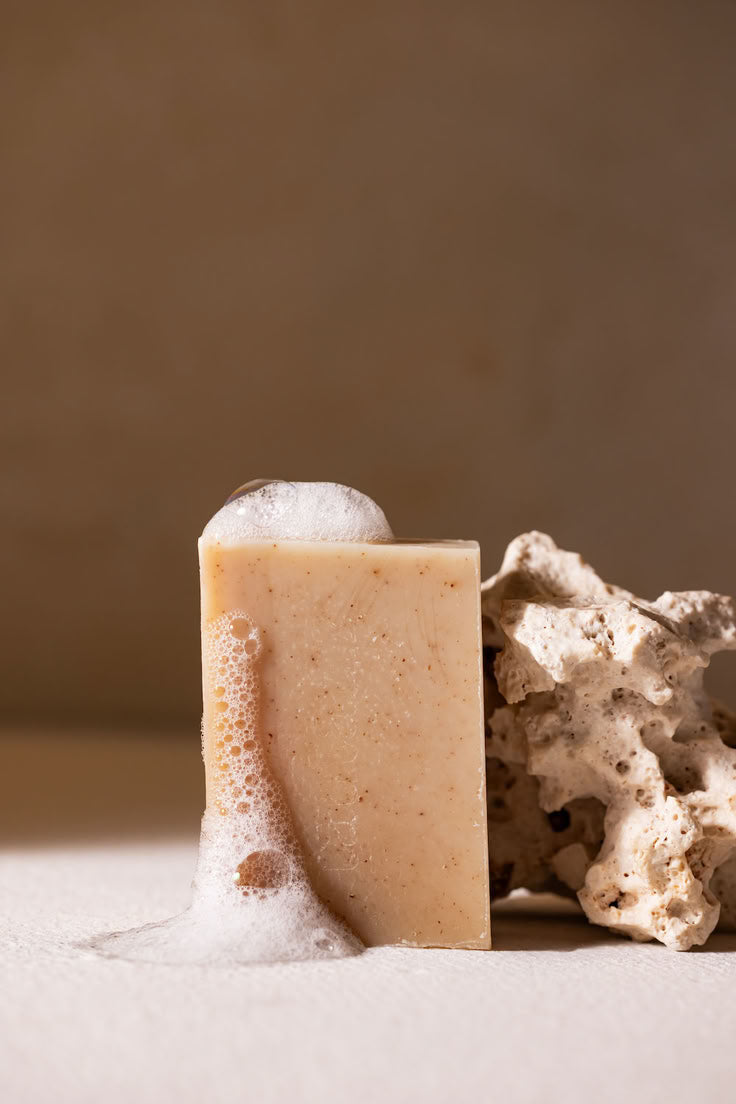Bar of soap with foam and coral on a neutral background